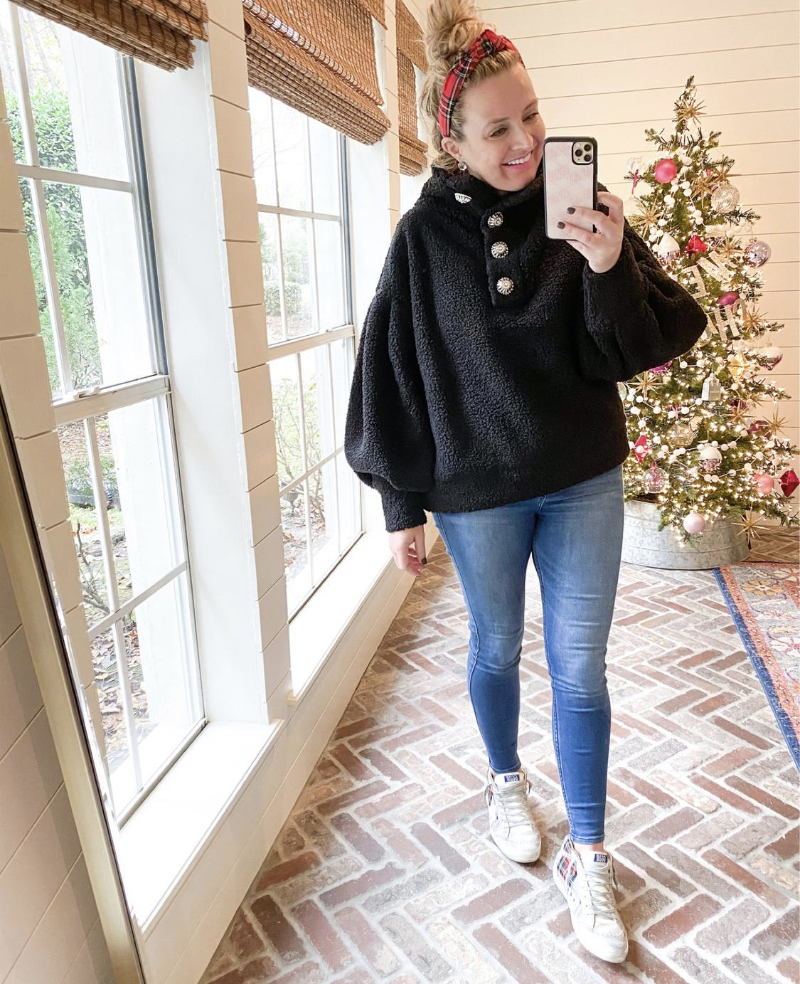 December Outfits by popular Houston fashion blog, Fancy Ashley: image of a woman standing in front of a Christmas tree decorated with pink, white and silver ornaments and wearing a black sherpa bubble sleeve top, jeans, and Golden Goose Sneakers. 