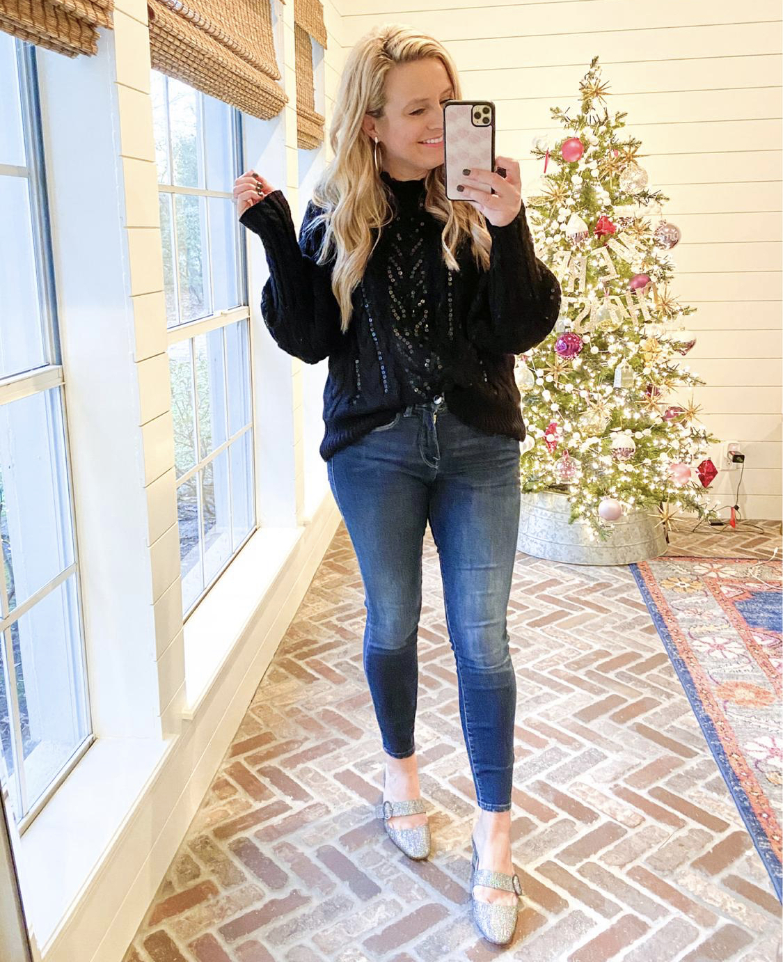 December Outfits by popular Houston fashion blog, Fancy Ashley: image of a woman standing in front of a Christmas tree decorated with pink, white and silver ornaments and wearing a black sequin sweater, jeans, and Sarah Jessica Parker sliver slide heel shoes. 