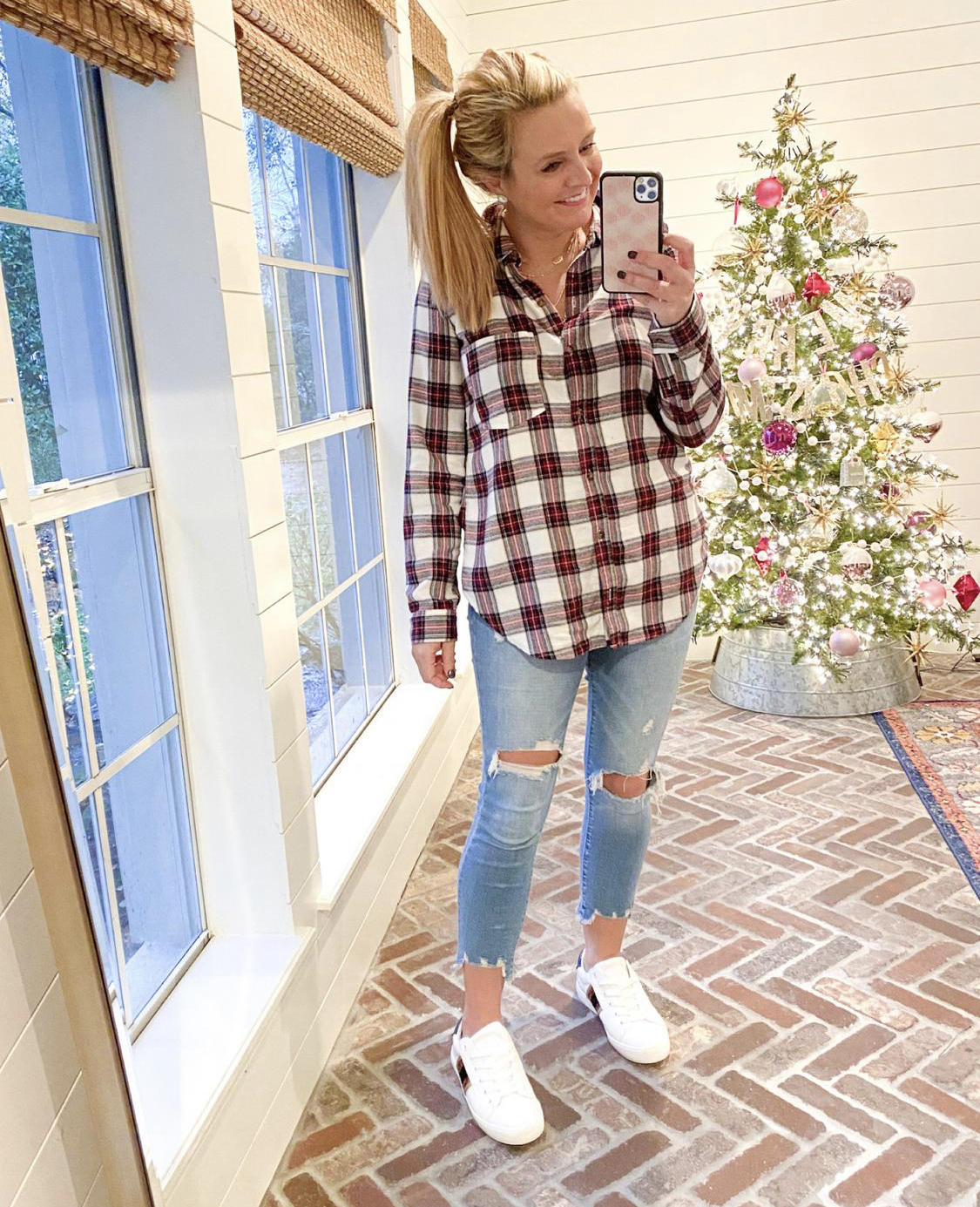 December Outfits by popular Houston fashion blog, Fancy Ashley: image of a woman standing in front of a Christmas tree decorated with pink, white and silver ornaments and wearing a red and white plaid button up shirt, distressed denim, and white sneakers. 