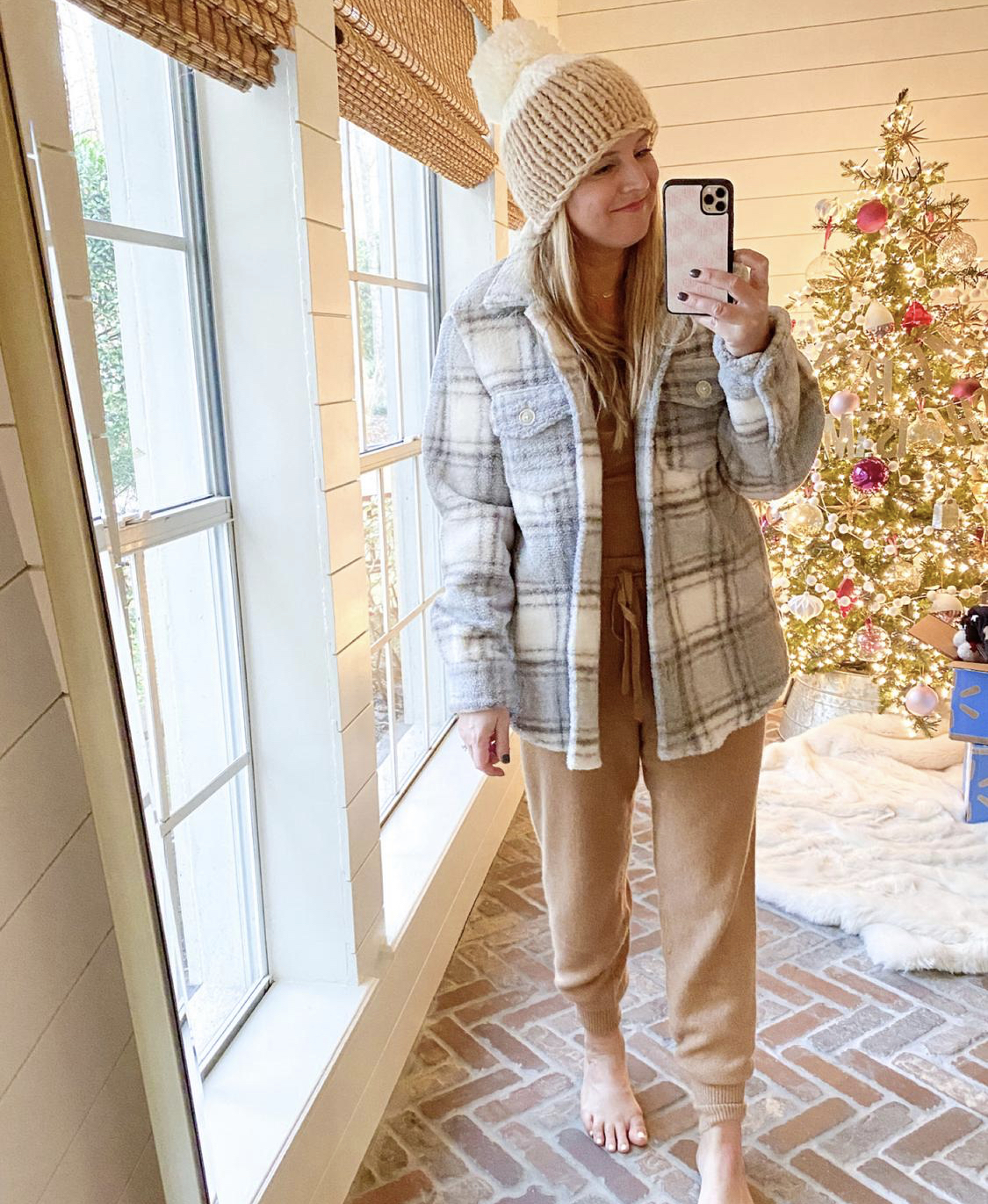 December Outfits by popular Houston fashion blog, Fancy Ashley: image of a woman standing in front of a Christmas tree decorated with pink, white and silver ornaments and wearing a tan and white pom beaning, tan sweater set, and grey and white plaid fleece jacket. 