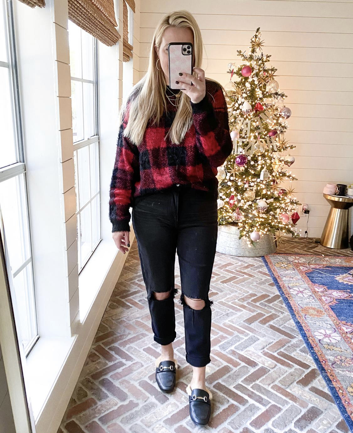 December Outfits by popular Houston fashion blog, Fancy Ashley: image of a woman standing in front of a Christmas tree decorated with pink, white and silver ornaments and wearing a red and black buffalo plaid shirt, black distressed jeans, and a black faux fur lined slide mules. 