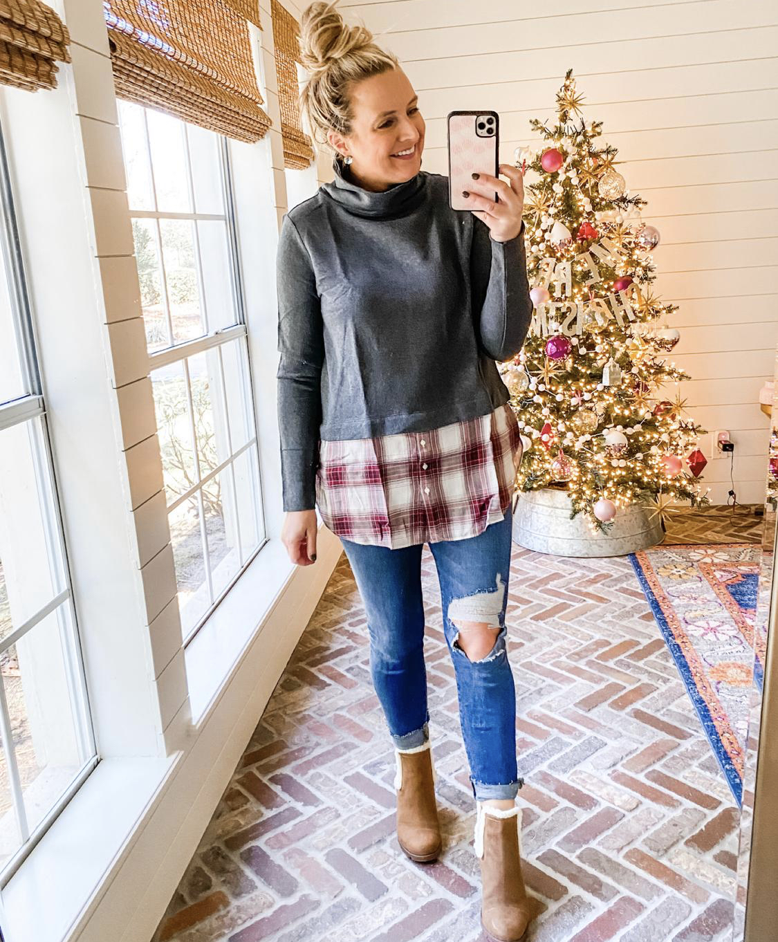 December Outfits by popular Houston fashion blog, Fancy Ashley: image of a woman standing in front of a Christmas tree decorated with pink, white and silver ornaments and wearing a grey and red and white plaid turtleneck shirt, distressed denim, and fur lined brown sueded ankle boots. 