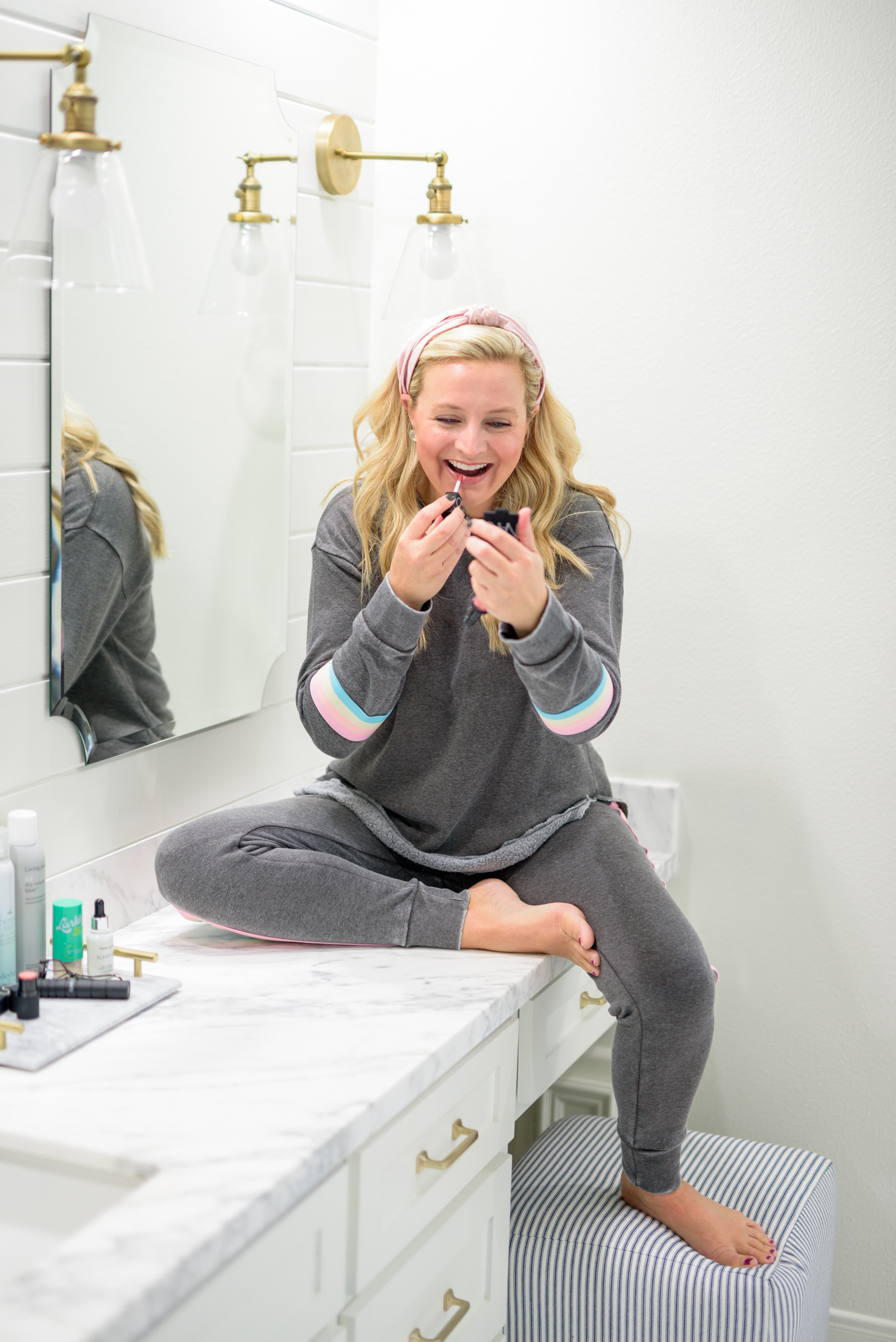 Fall Beauty by popular Houston beauty blog, Fancy Ashley: image of a woman sitting on her bathroom vanity and wearing a Burnout Stripe Sweatshirt VINTAGE HAVANA and Burnout Stripe Joggers VINTAGE HAVANA and applying lipgloss. 