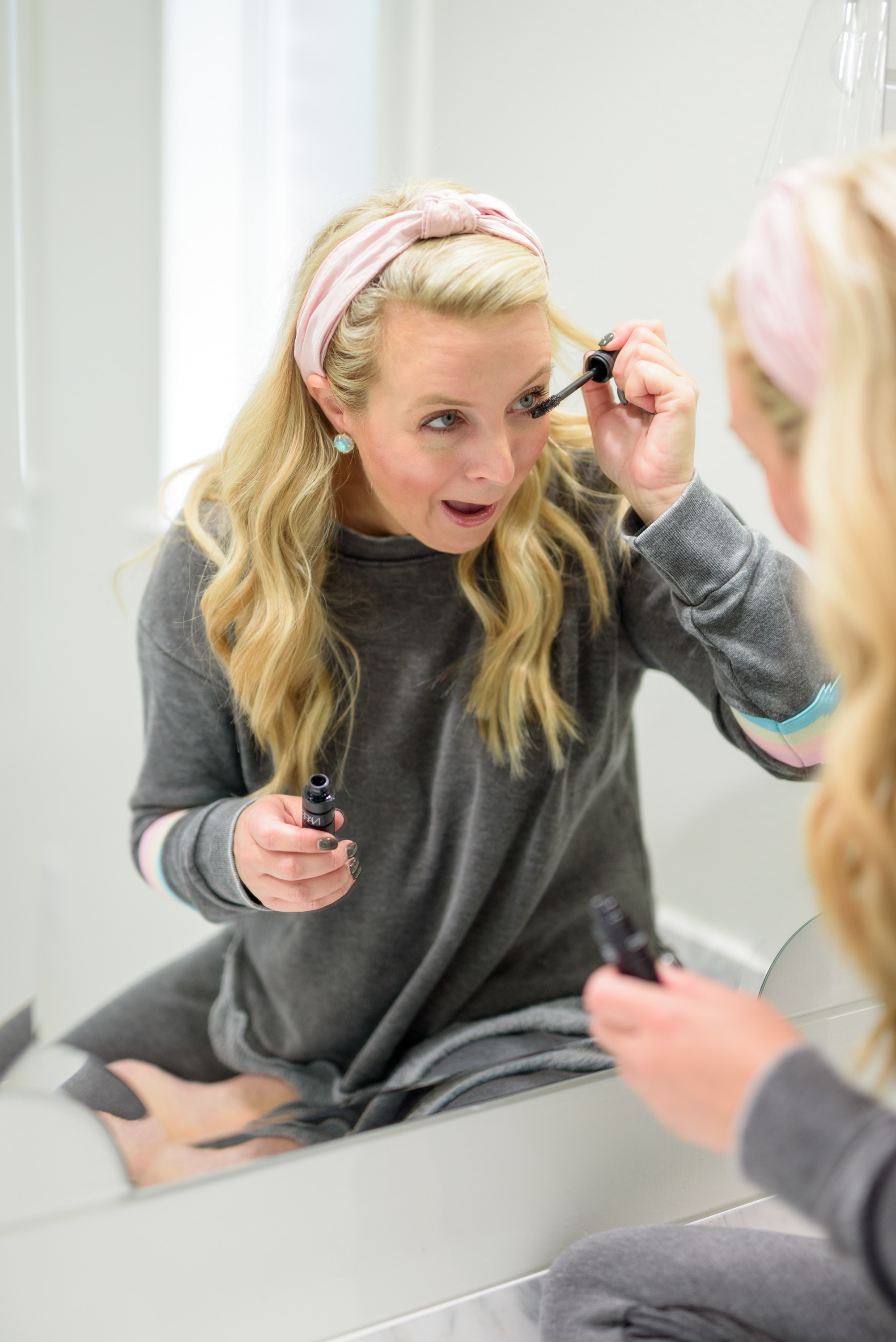 Fall Beauty by popular Houston beauty blog, Fancy Ashley: image of a woman sitting on her bathroom vanity and wearing a Burnout Stripe Sweatshirt VINTAGE HAVANA and Burnout Stripe Joggers VINTAGE HAVANA and applying mascara.