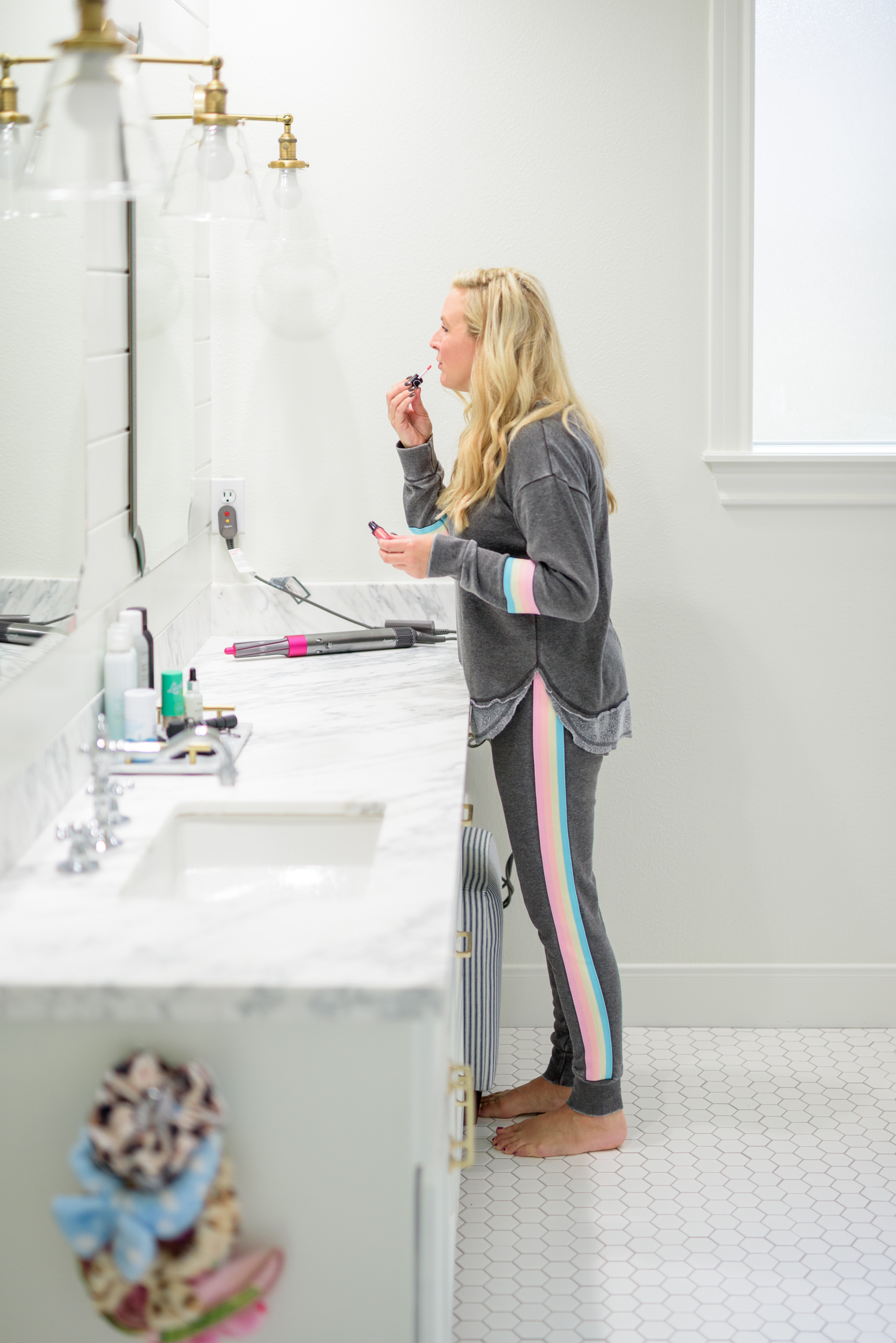 Fall Beauty by popular Houston beauty blog, Fancy Ashley: image of a woman sitting on her bathroom vanity and wearing a Burnout Stripe Sweatshirt VINTAGE HAVANA and Burnout Stripe Joggers VINTAGE HAVANA and using Nars lipgloss. 