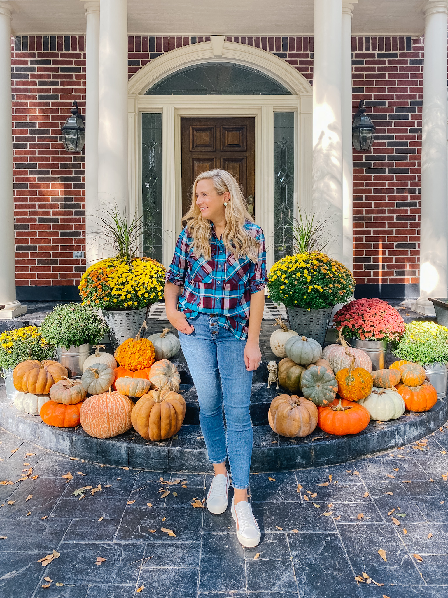 Fall Plaid by popular Houston fashion blog, Fancy Ashley: image of a woman standing in front of a front porch decorated with pumpkins and potted mums and wearing a plaid top, jeans, and white sneakers. 