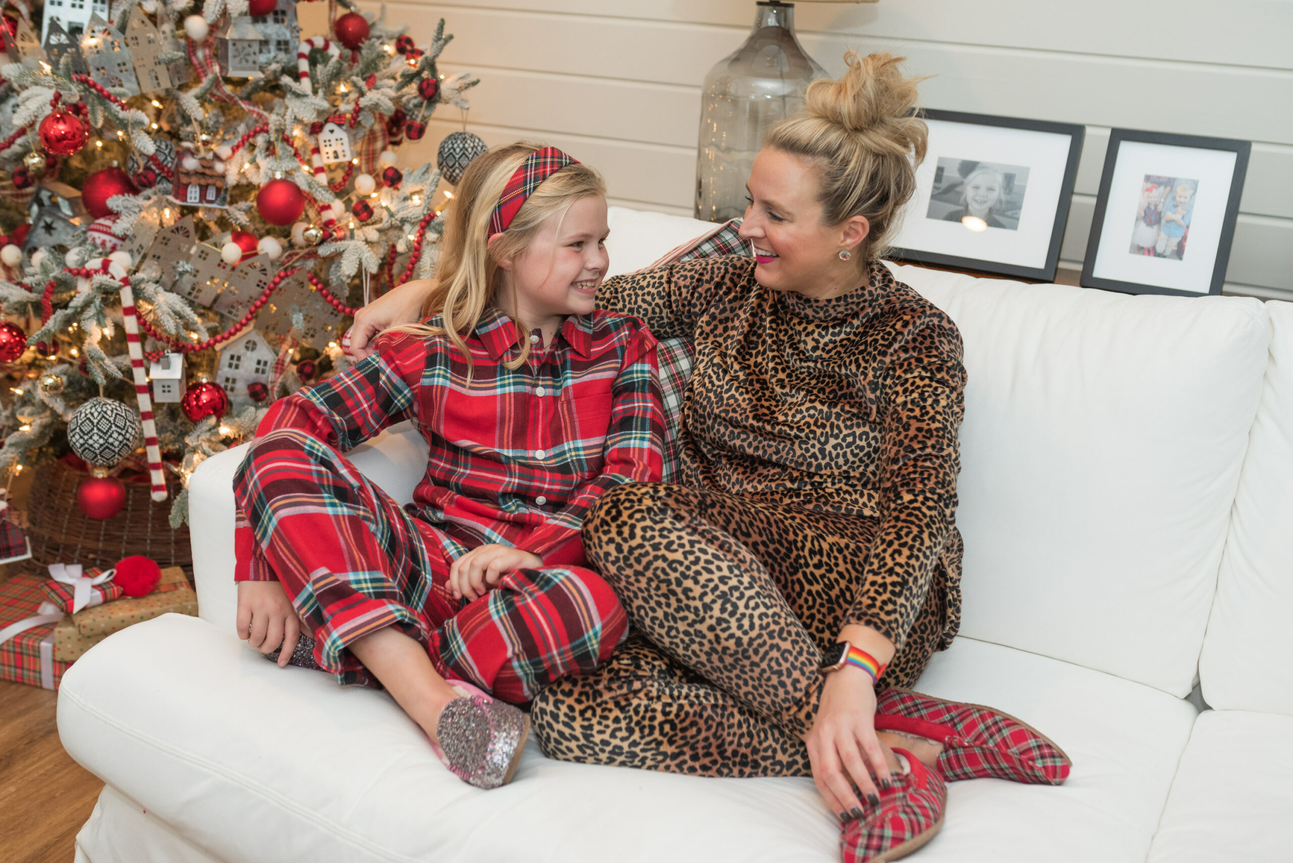 Family Christmas Pajamas by popular Houston fashion blog, Fancy Ashley: image of a mom and her young daughter sitting on a white couch and wearing Land's End leopard print and red plaid pajamas and glitter and red plaid moccasin slippers. 