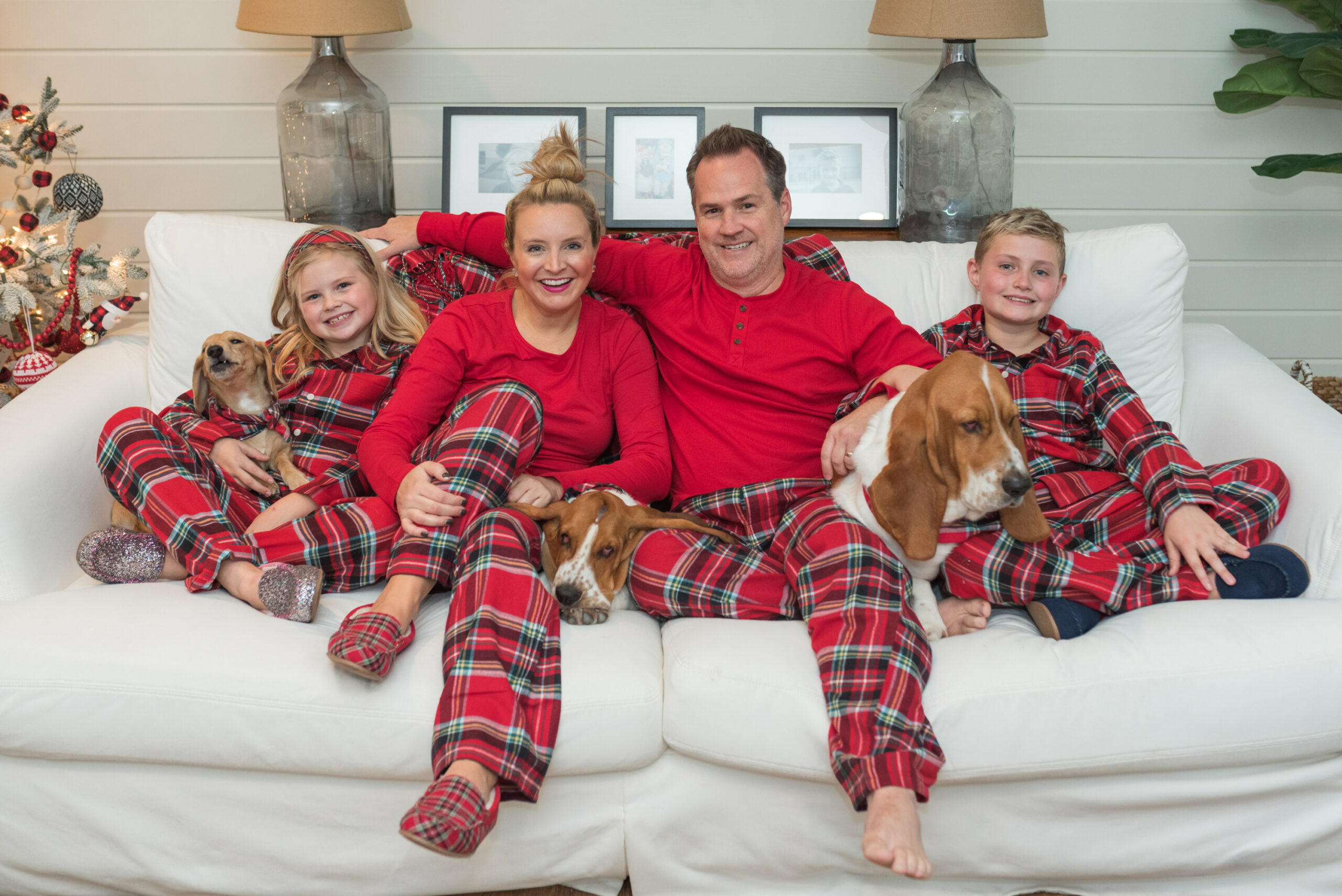 Family Christmas Pajamas by popular Houston fashion blog, Fancy Ashley: image of a family sitting on a white couch with their three dogs and wearing matching red plaid pajamas from Land's End. 