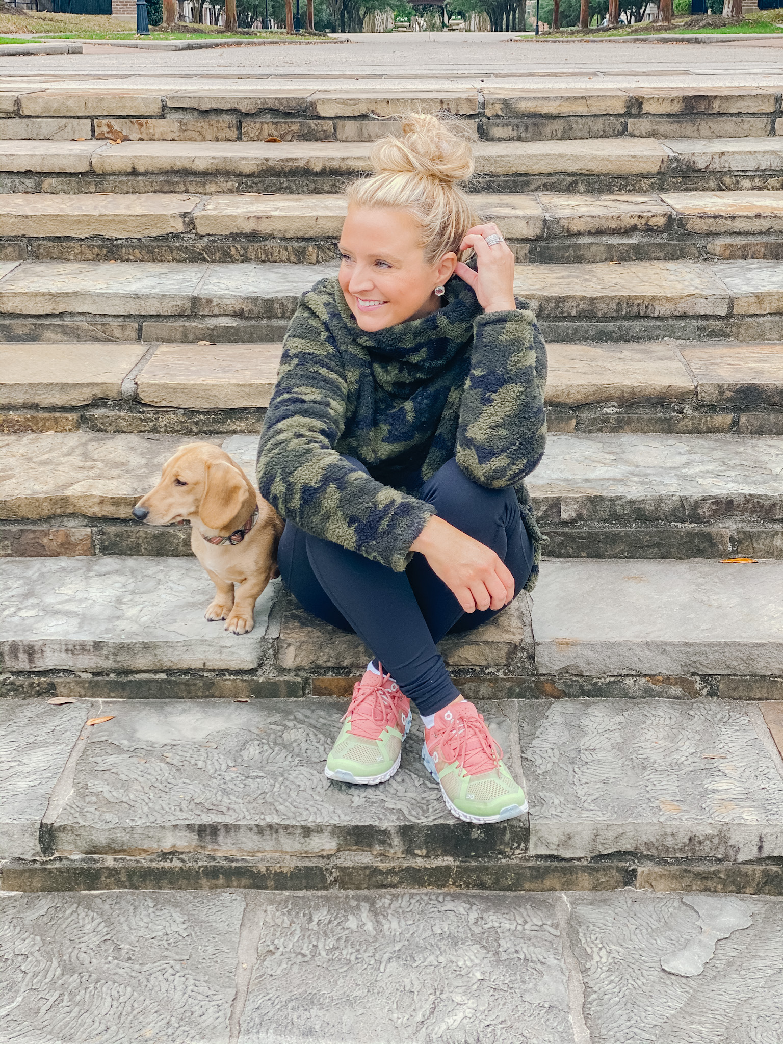 On Cloud Running Shoes by popular Houston fashion blog, Fancy Ashley: image of a woman sitting on some stone steps with her dog and wearing Shoes Cloudflow Running Shoes, Zella leggings, Zella camo fleece pullover, and Quay Australia sunglasses. 