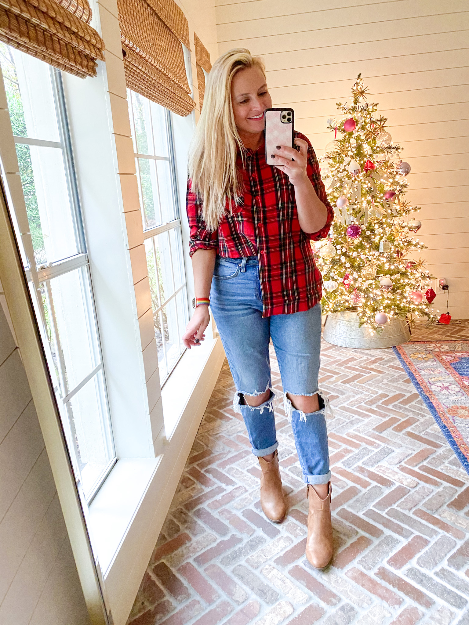 December Outfits by popular Houston fashion blog, Fancy Ashley: image of a woman standing in front of a Christmas tree decorated with pink, white and silver ornaments and wearing a red and green plaid button up top, distressed denim, and tan ankle boots. 