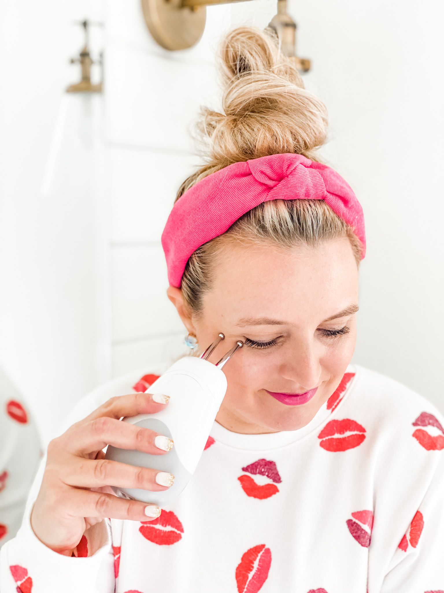 NuFace Trinity by popular Houston beauty blog, Fancy Ashley: image of a woman wearing a lip print pajama set and siting on her bathroom counter while using the NuFace Trinity facial toner. 