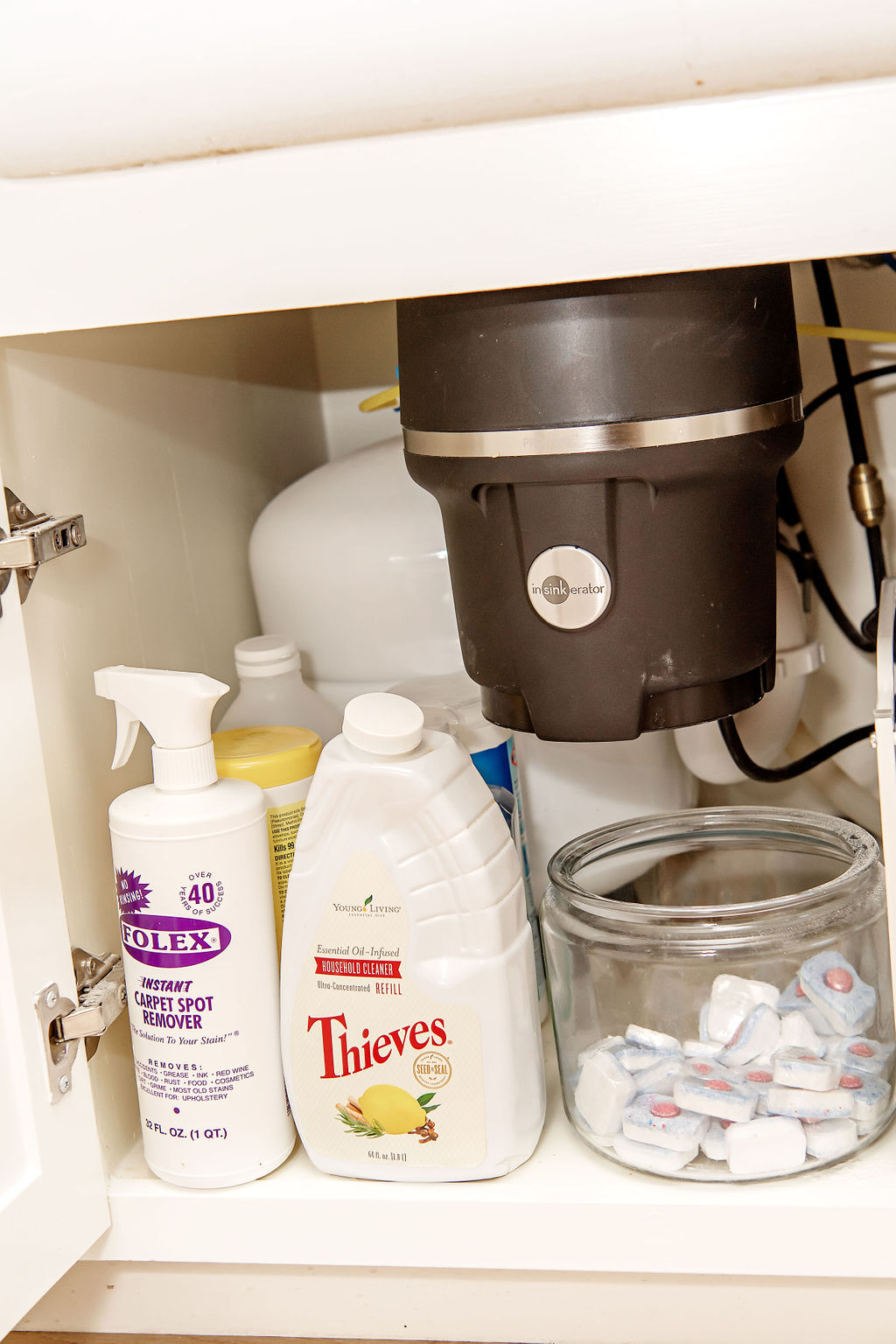 Under Bathroom Sink Organization by popular Houston lifestyle blog, Fancy Ashley: image of a bathroom under sink cabinet containing Thieve cleaning solution and a glass canister filled with dishwasher pods. 