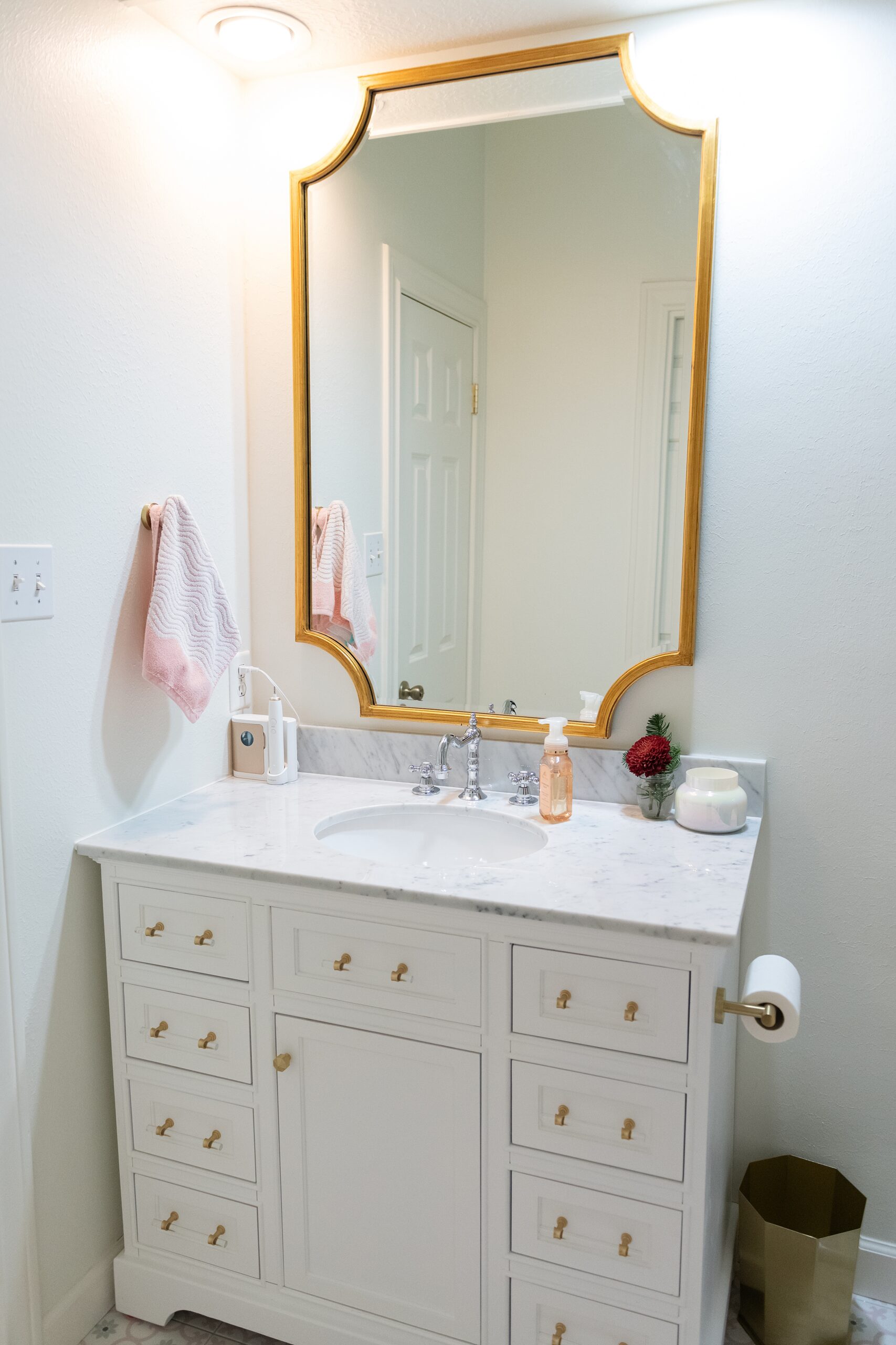 Girls Bathroom by popular Houston life and style blog, Fancy Ashley: image of a bathroom with pink and grey tile, white vanity with marble counter top and gold drawer pulls, and gold frame mirror. 