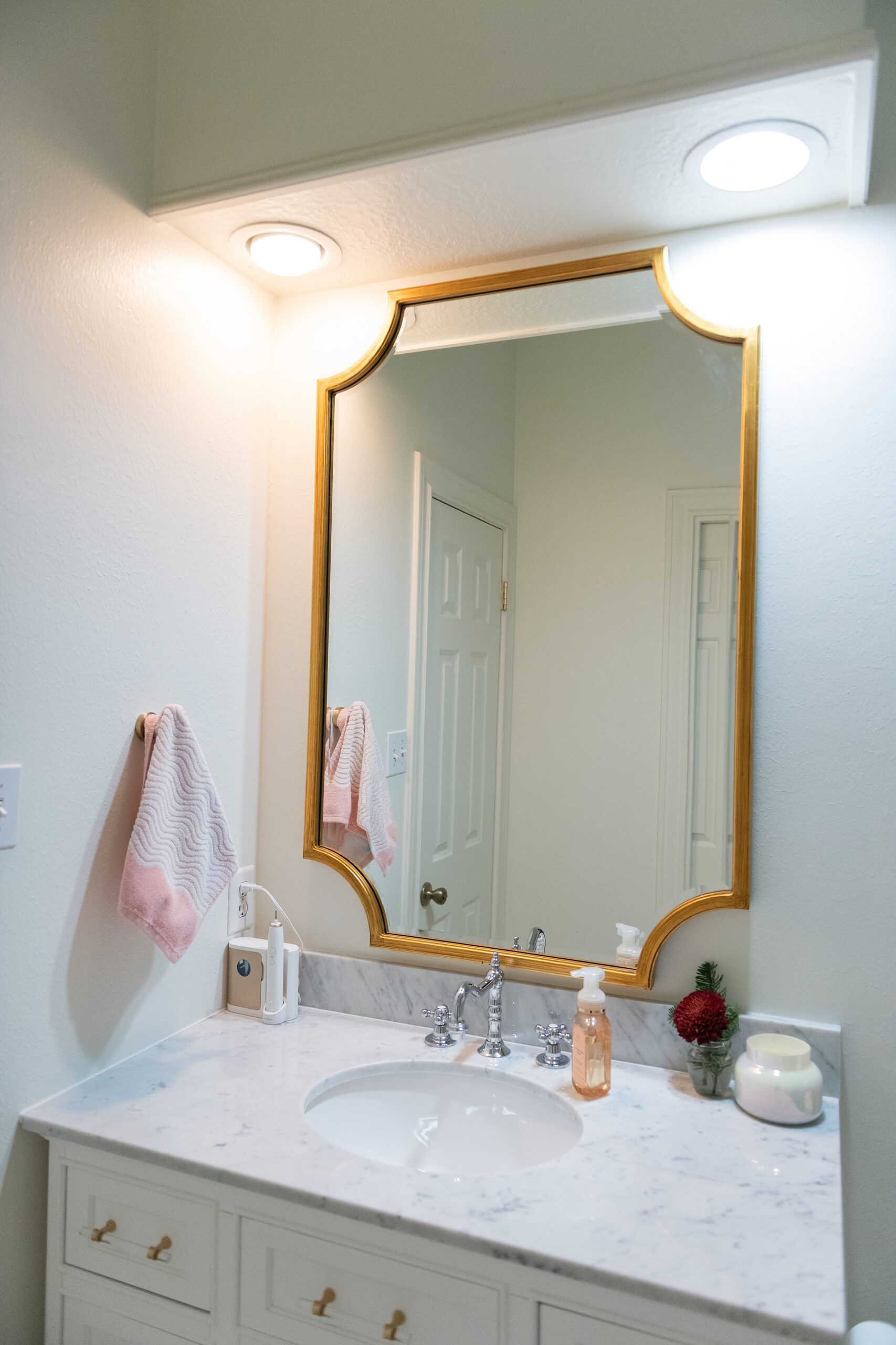 Girls Bathroom by popular Houston life and style blog, Fancy Ashley: image of a bathroom with pink and grey tile, white vanity with marble counter top and gold drawer pulls, and gold frame mirror. 