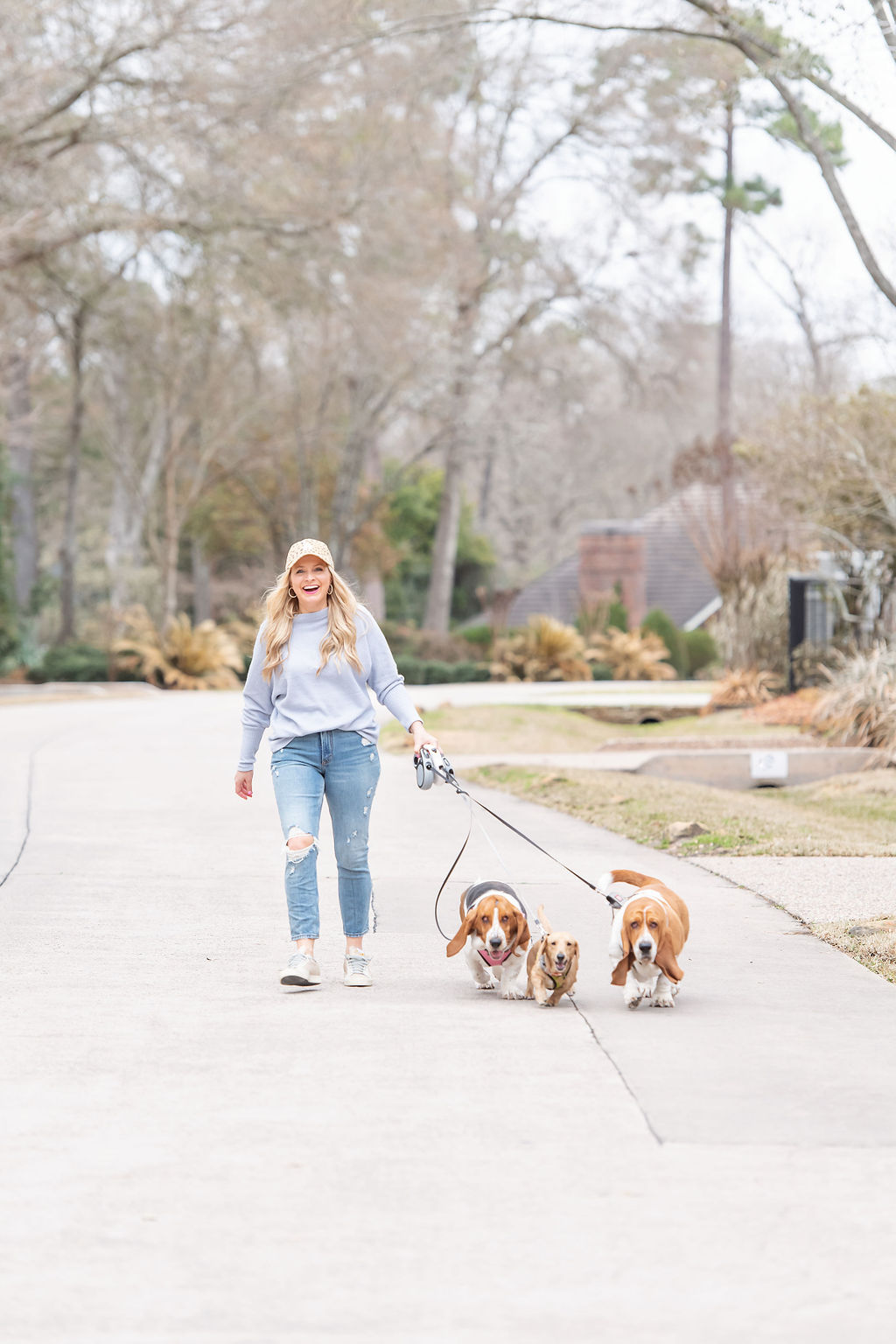 International Women's Day with Gibson by popular Houston fashion blog, Fancy Ashley: image of a woman wearing a Gibson grey Fancy Ashley sweater with distressed jeans, sneakers, and a baseball cap while walking her dogs.  