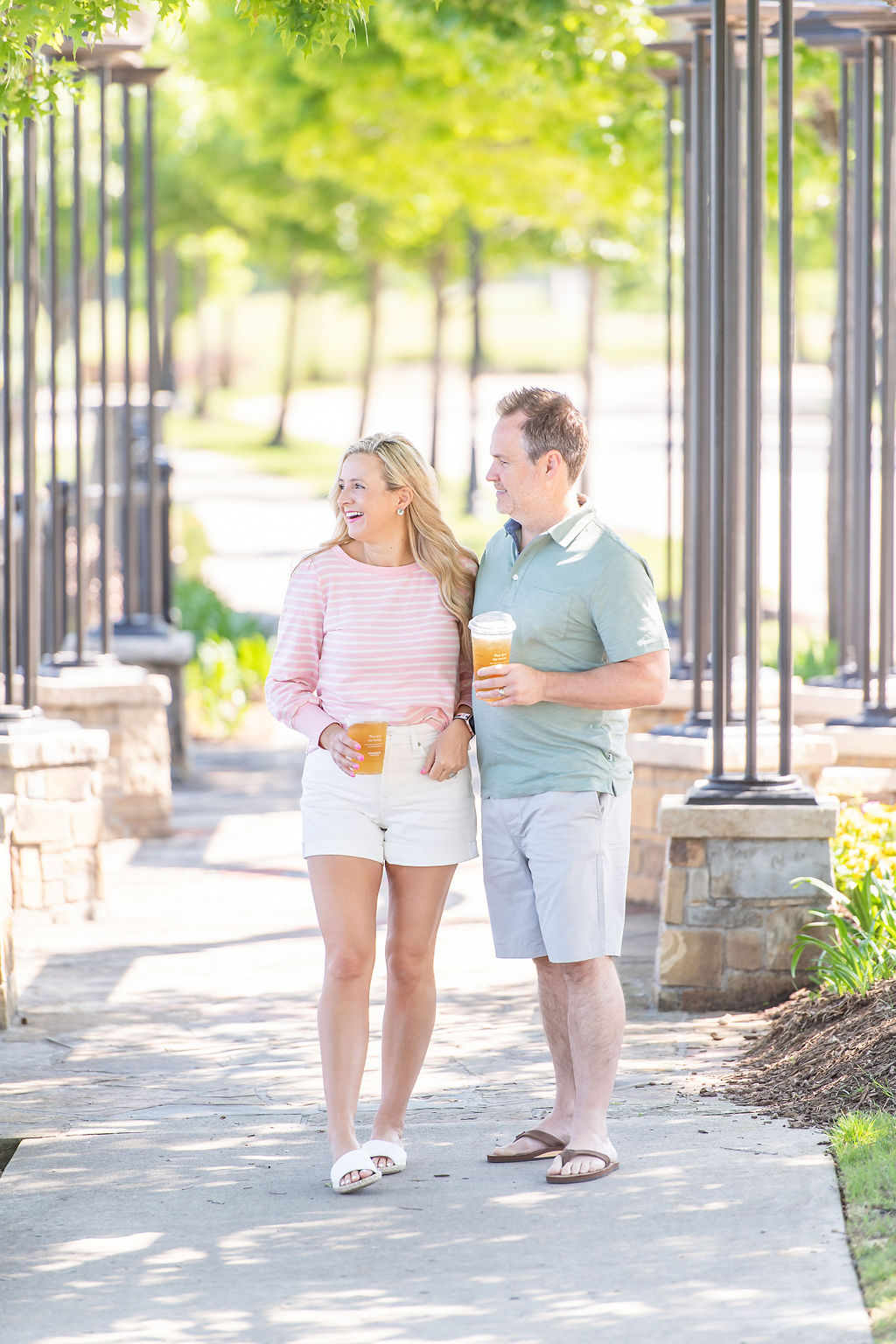 Walmart Summer Fashion by popular Houston fashion blog, The House of Fancy: image of a husband and wife standing together and wearing a pink and white stripe long sleeve top, white, shorts, white slide sandals, green polo, grey shorts and tan thong sandals. 