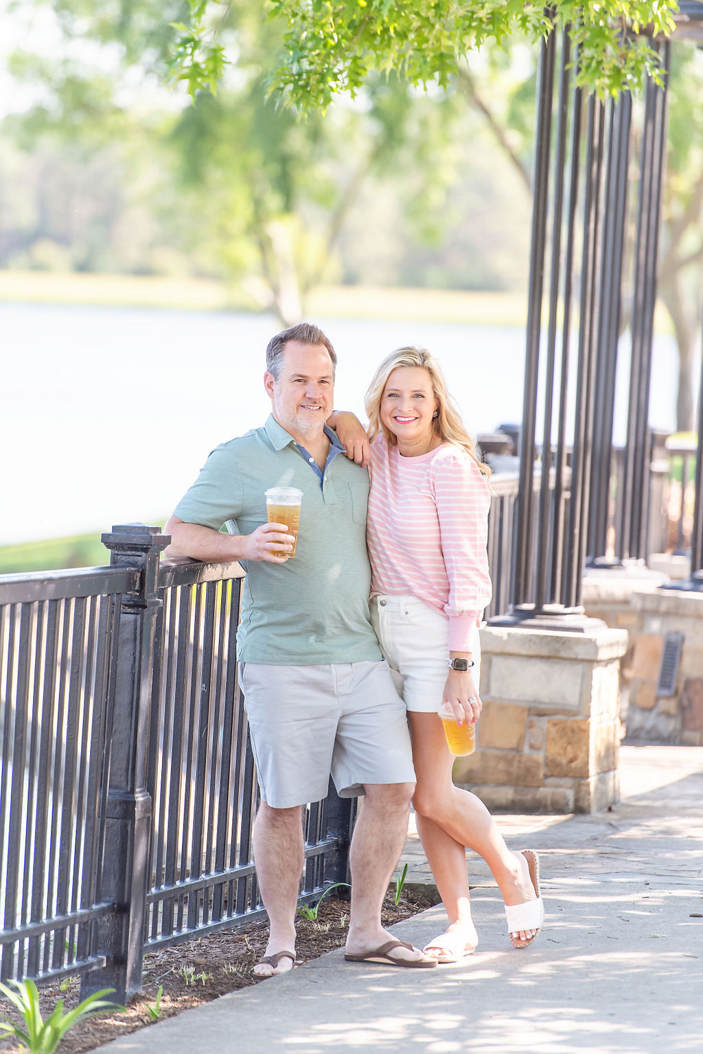 Walmart Summer Fashion by popular Houston fashion blog, The House of Fancy: image of a husband and wife standing together and wearing a pink and white stripe long sleeve top, white, shorts, white slide sandals, green polo, grey shorts and tan thong sandals. 