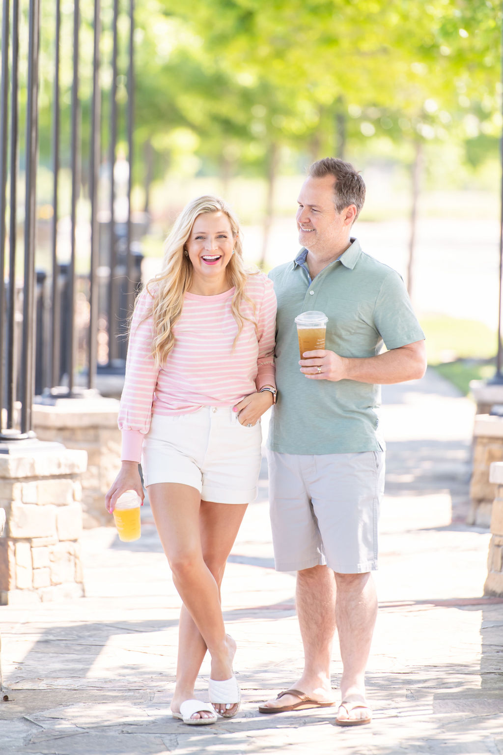 Walmart Summer Fashion by popular Houston fashion blog, The House of Fancy: image of a husband and wife standing together and wearing a pink and white stripe long sleeve top, white, shorts, white slide sandals, green polo, grey shorts and tan thong sandals. 