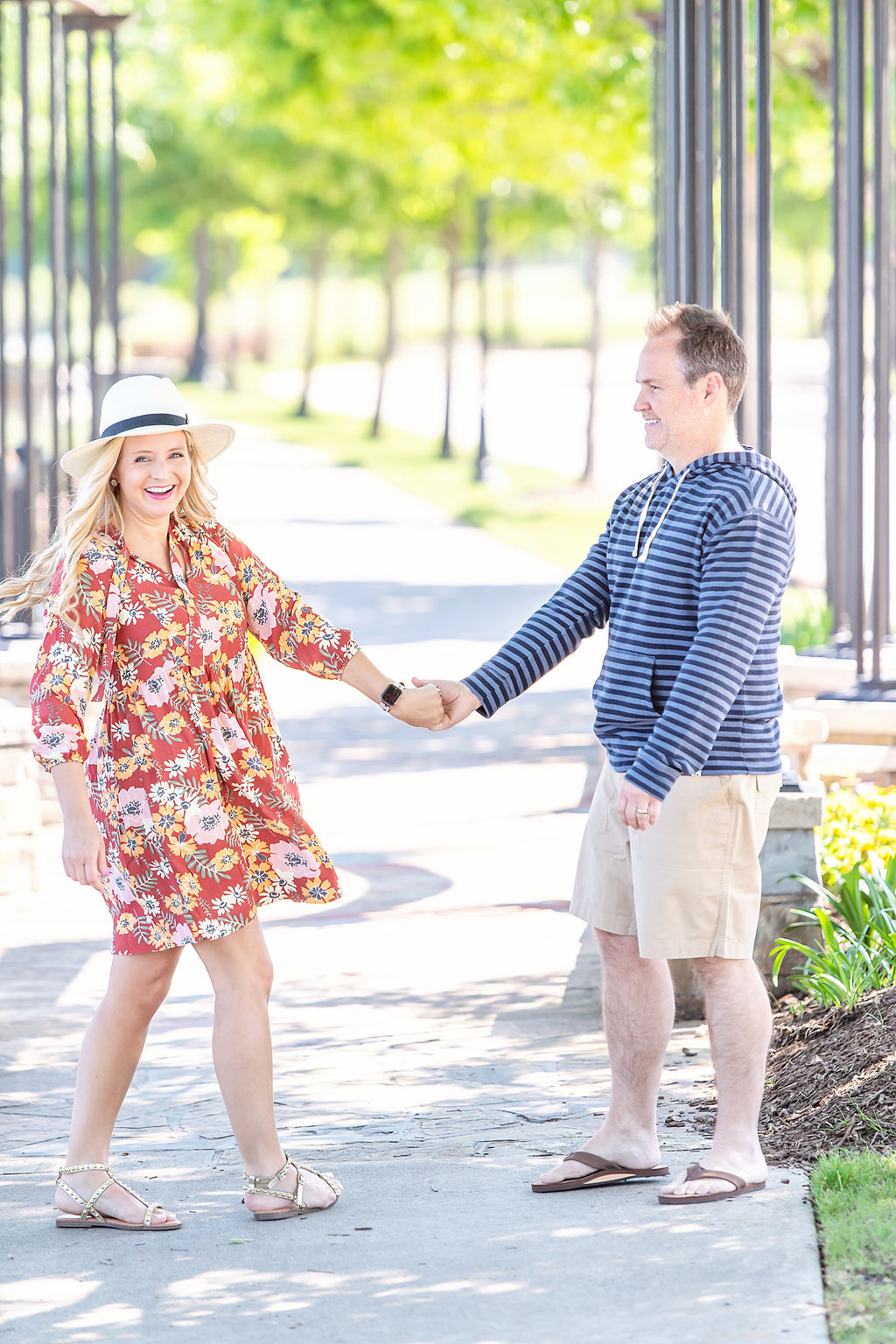 Walmart Summer Fashion by popular Houston fashion blog, The House of Fancy: image of a husband and wife standing together and wearing a red floral print dress, straw sun hat, studded gold strap sandals, brown thong sandals, blue stipe hoodie sweatshirt, and tan shorts. 