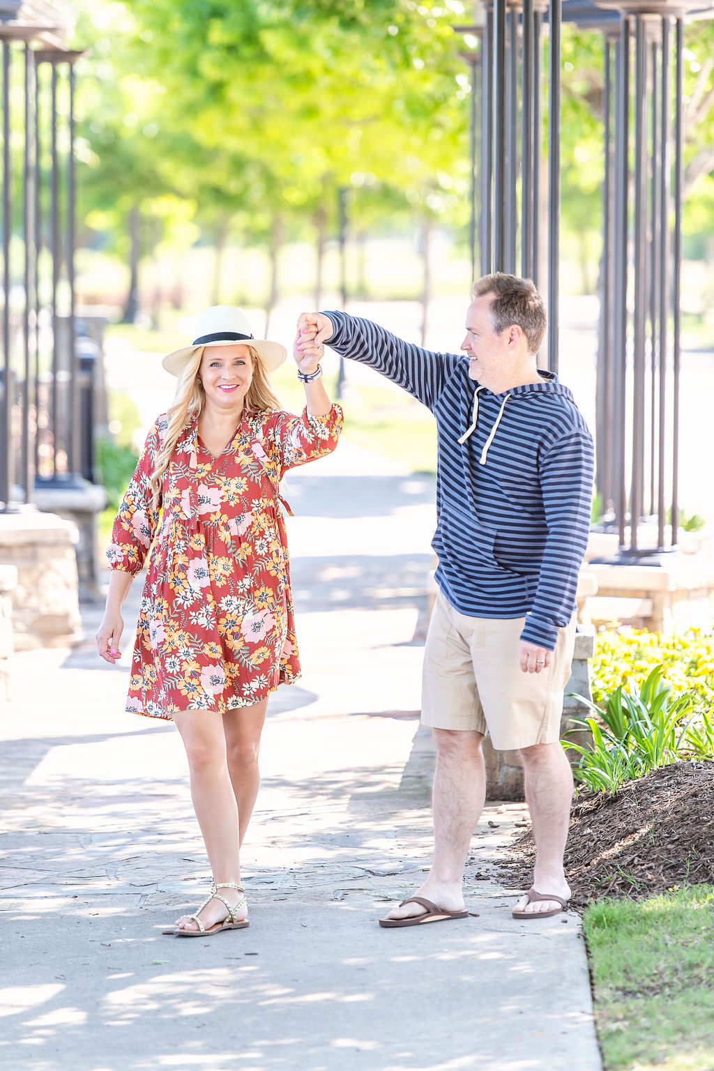 Walmart Summer Fashion by popular Houston fashion blog, The House of Fancy: image of a husband and wife standing together and wearing a red floral print dress, straw sun hat, studded gold strap sandals, brown thong sandals, blue stipe hoodie sweatshirt, and tan shorts. 