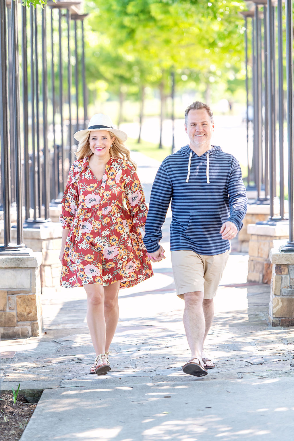 Walmart Summer Fashion by popular Houston fashion blog, The House of Fancy: image of a husband and wife standing together and wearing a red floral print dress, straw sun hat, studded gold strap sandals, brown thong sandals, blue stipe hoodie sweatshirt, and tan shorts. 