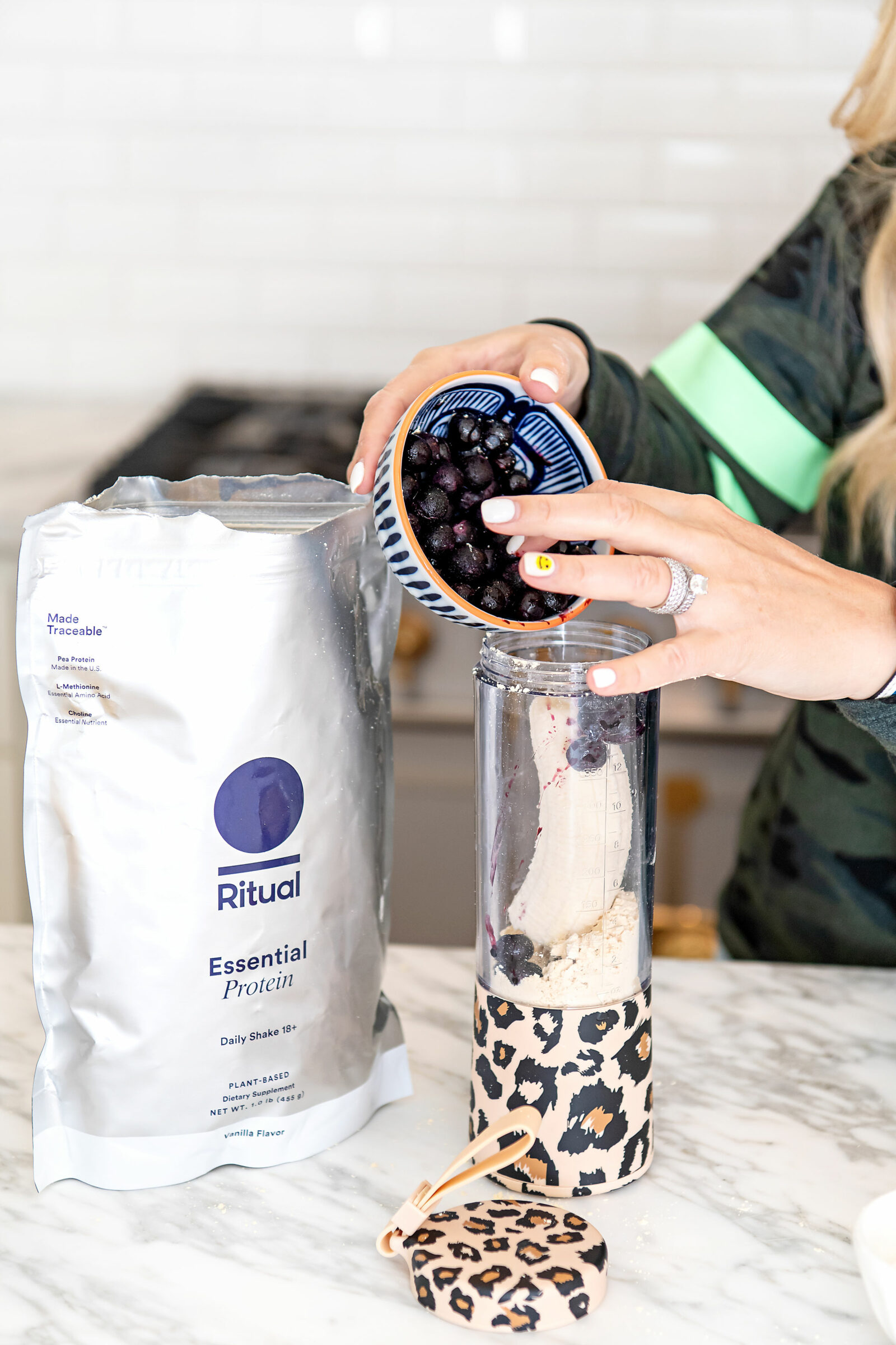 Healthy Living by popular Houston lifestyle blog, The House of Fancy: image of a woman wearing a camo top and putting ritual powder, blueberries and a banana in a leopard print cup. 