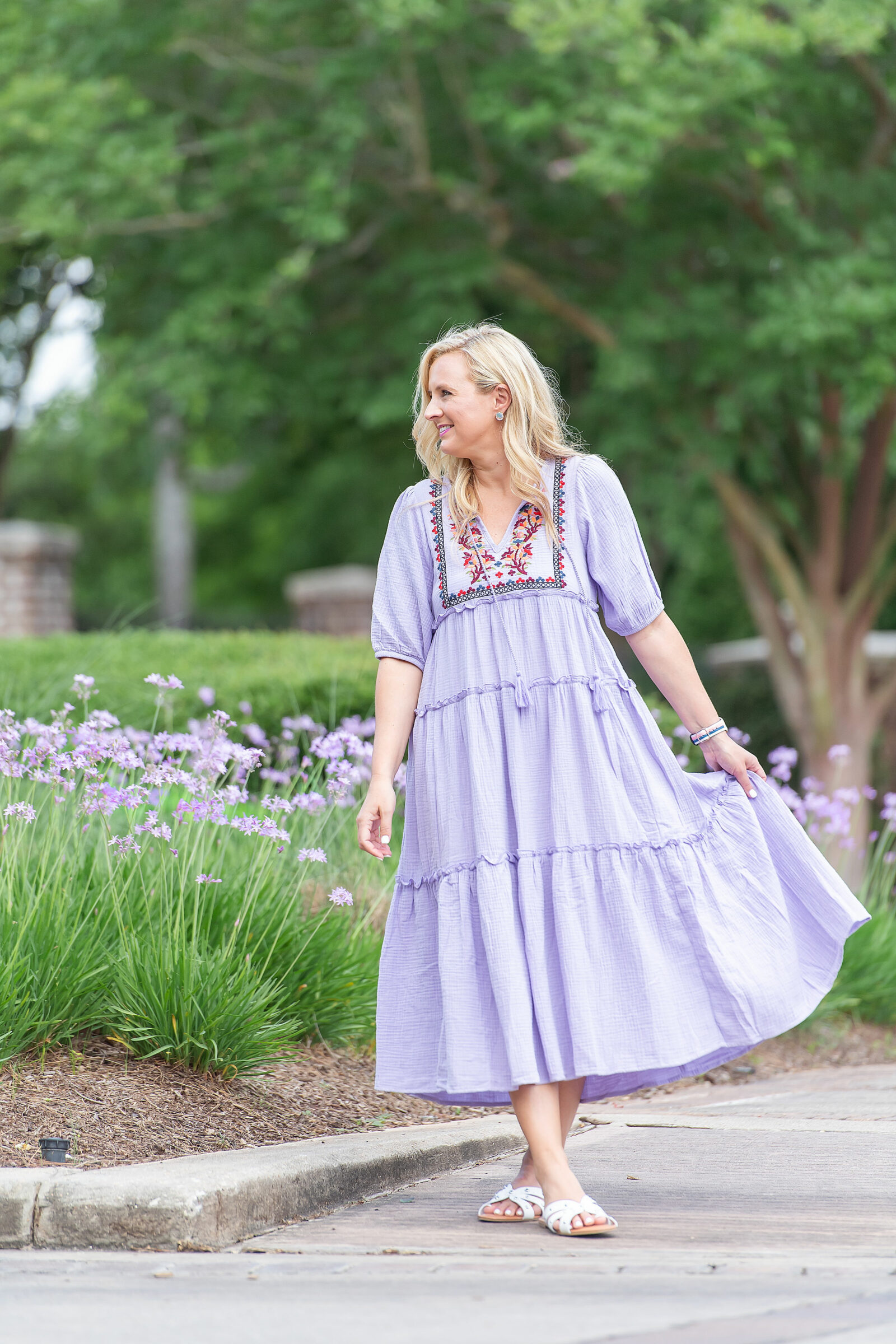 Prettiest Embroidered Dresses for Summer | Embroidered Dresses by popular Houston fashion blog, The House of Fancy: image of a woman standing by some purple flowers and wearing a floral embroidered purple tiered maxi dress. 