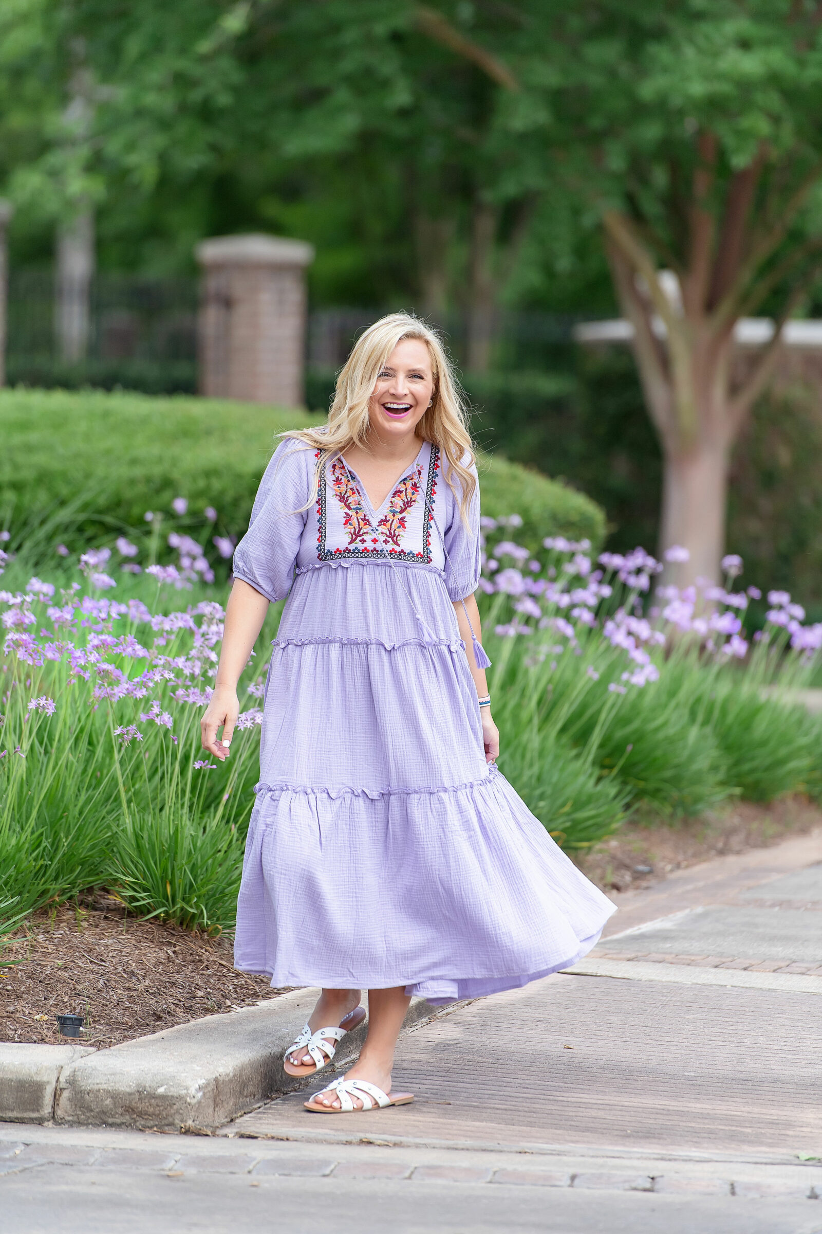 Prettiest Embroidered Dresses for Summer | Embroidered Dresses by popular Houston fashion blog, The House of Fancy: image of a woman standing by some purple flowers and wearing a floral embroidered purple tiered maxi dress. 