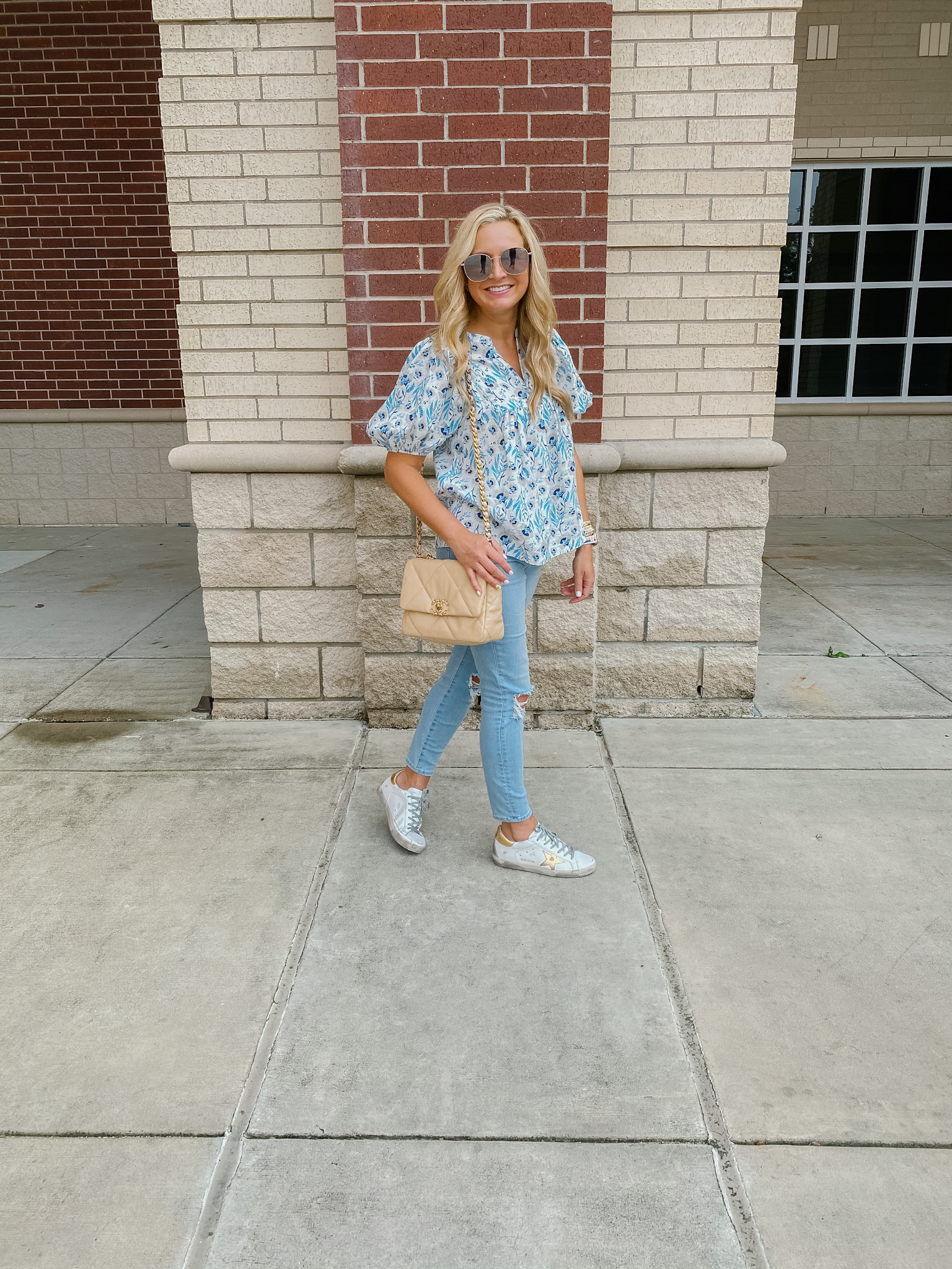 Best Sellers by popular Houston fashion blog, The House of Fancy: image of a woman standing next to a brick building and wearing a blue floral print puff sleeve top, light wash distress denim and golden goose sneakers. 