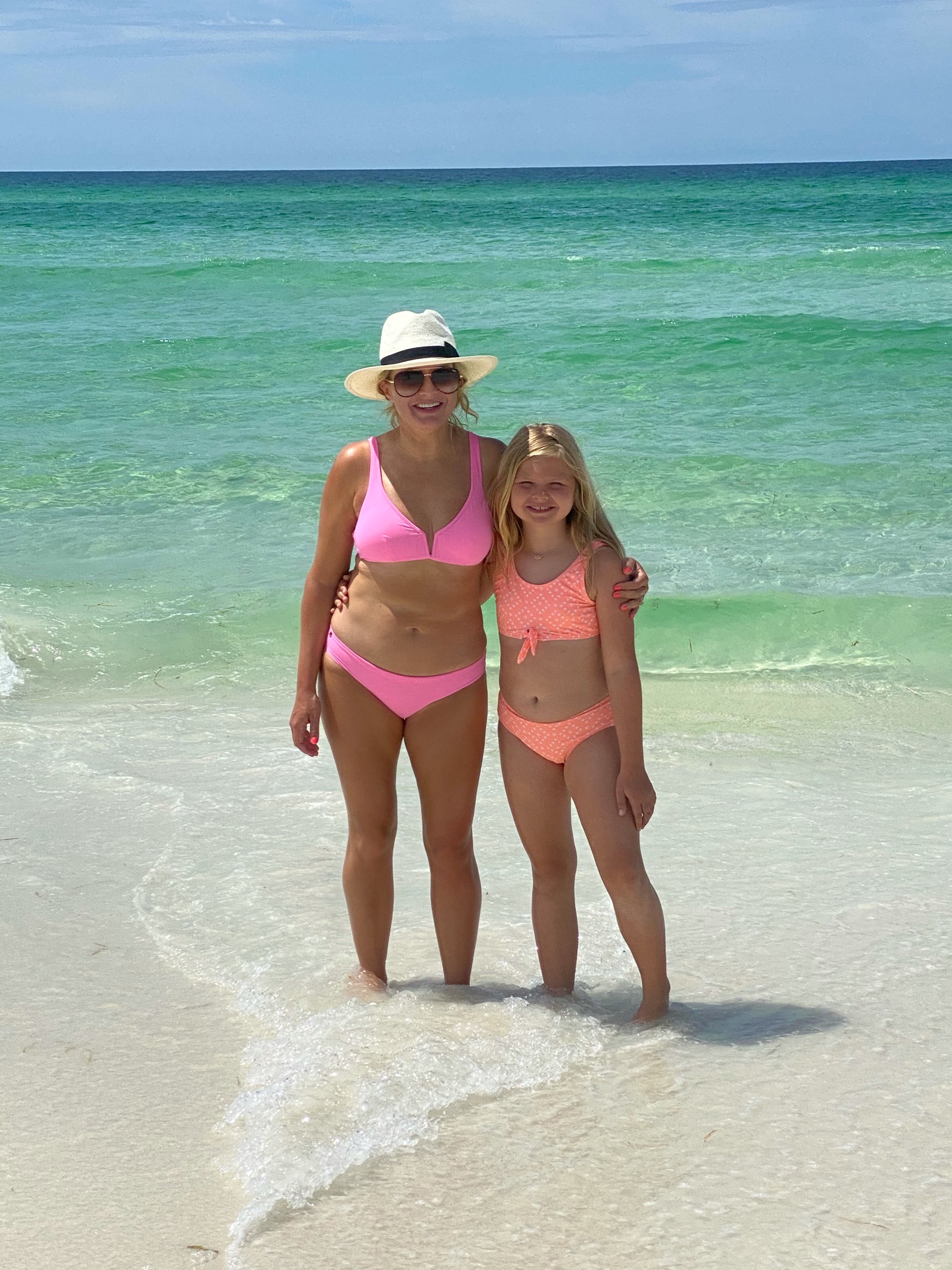 Seaside Florida by popular Houston travel blog, The House of Fancy: image of a mom and her young daughter standing together in the ocean and wearing a neon pink bikini, white straw fedora, and orange two piece swimsuit. 