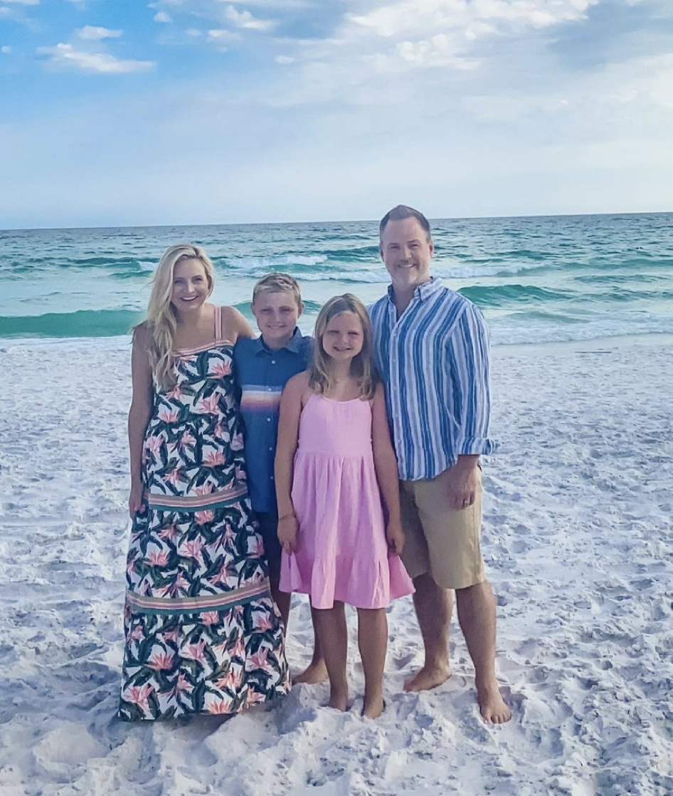 fancy Ashley family photo looks | Family Photo Outfits by popular Houston fashion blog, The House of Fancy: image of a family standing on a white sand beach and wearing a pink floral print maxi dress, pink tiered dress, blue stripe button up shirt, tan shorts, and blue button shirt with a multi color stripe accent.