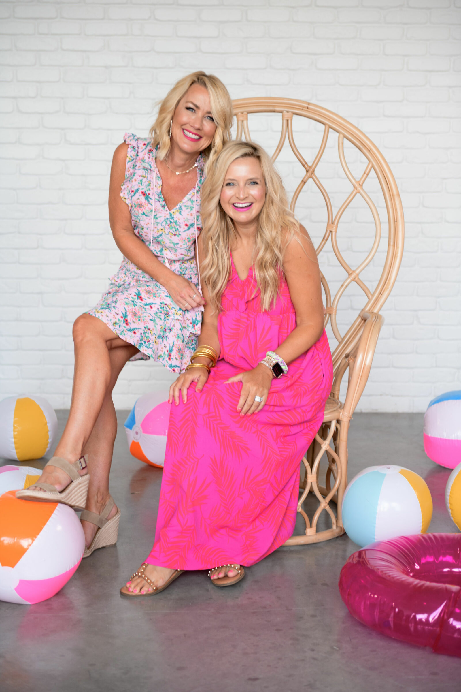 Best Sellers by popular Houston fashion blog, The House of Fancy: image of two women sitting together in a bamboo peacock chair and wearing a pink and red tropical print maxi dress and pink floral print refuel sleeve dress. 